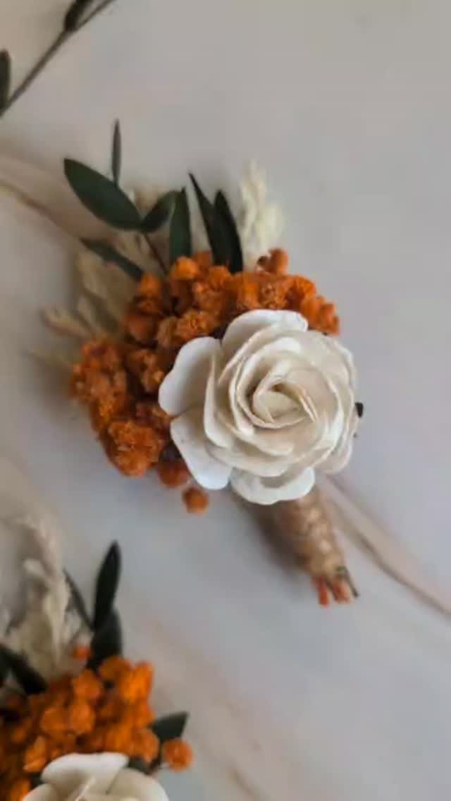 Boutonniere with a white rose and orange dried flowers wrapped in twine.