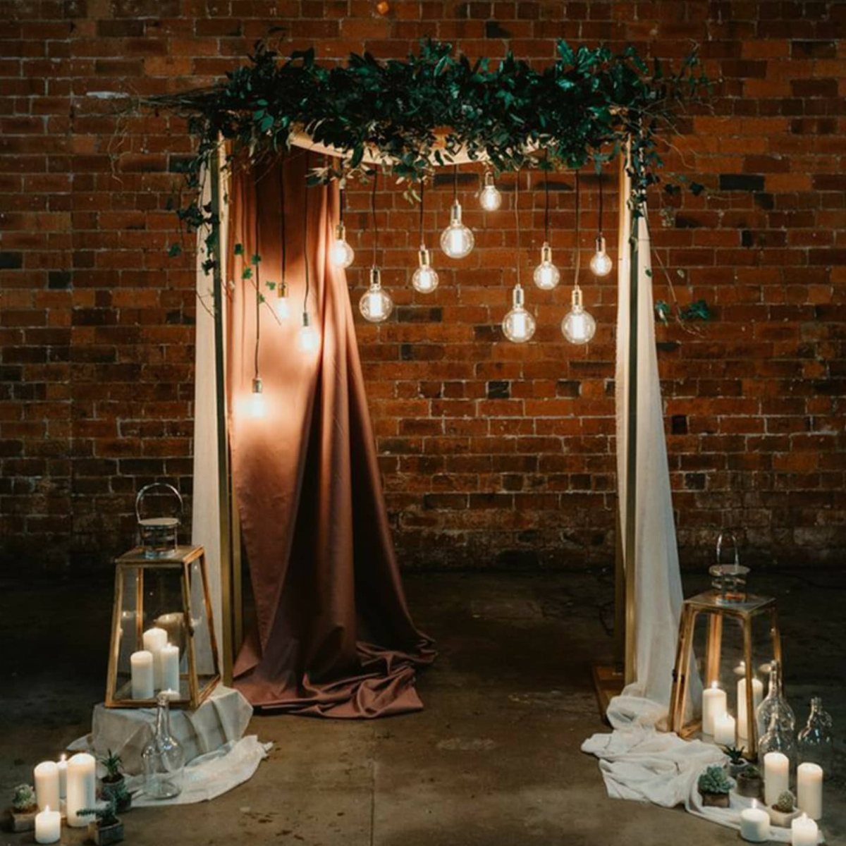 Decorative archway with hanging lights, terracotta fabric, and lanterns against a brick wall.