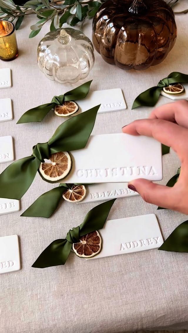 White embossed place cards tied with green ribbons and dried citrus slices on linen.