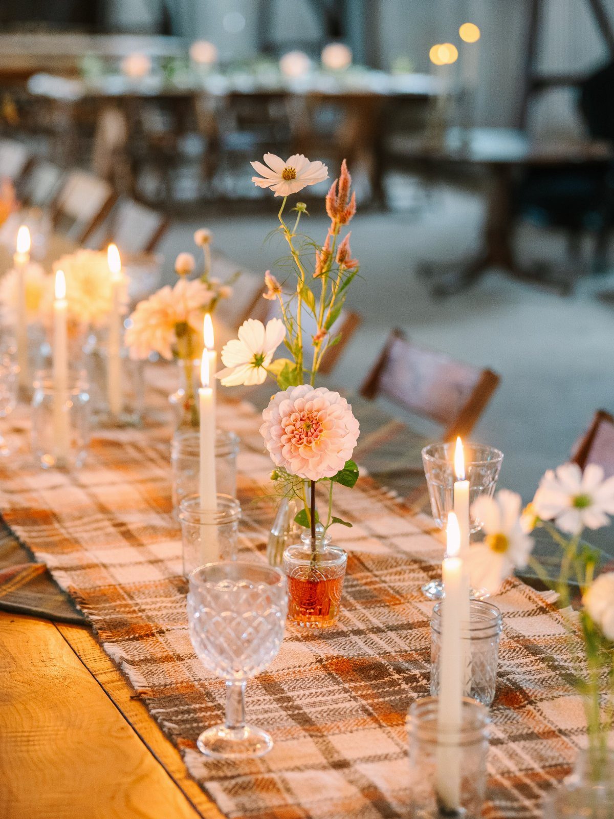 Brown and white plaid table runner with candles and floral centerpieces on wood.