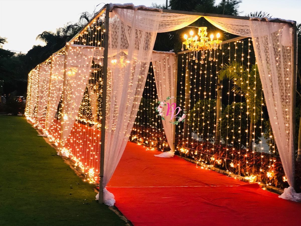 Red carpet walkway under a white draped canopy with hanging string lights and chandelier.