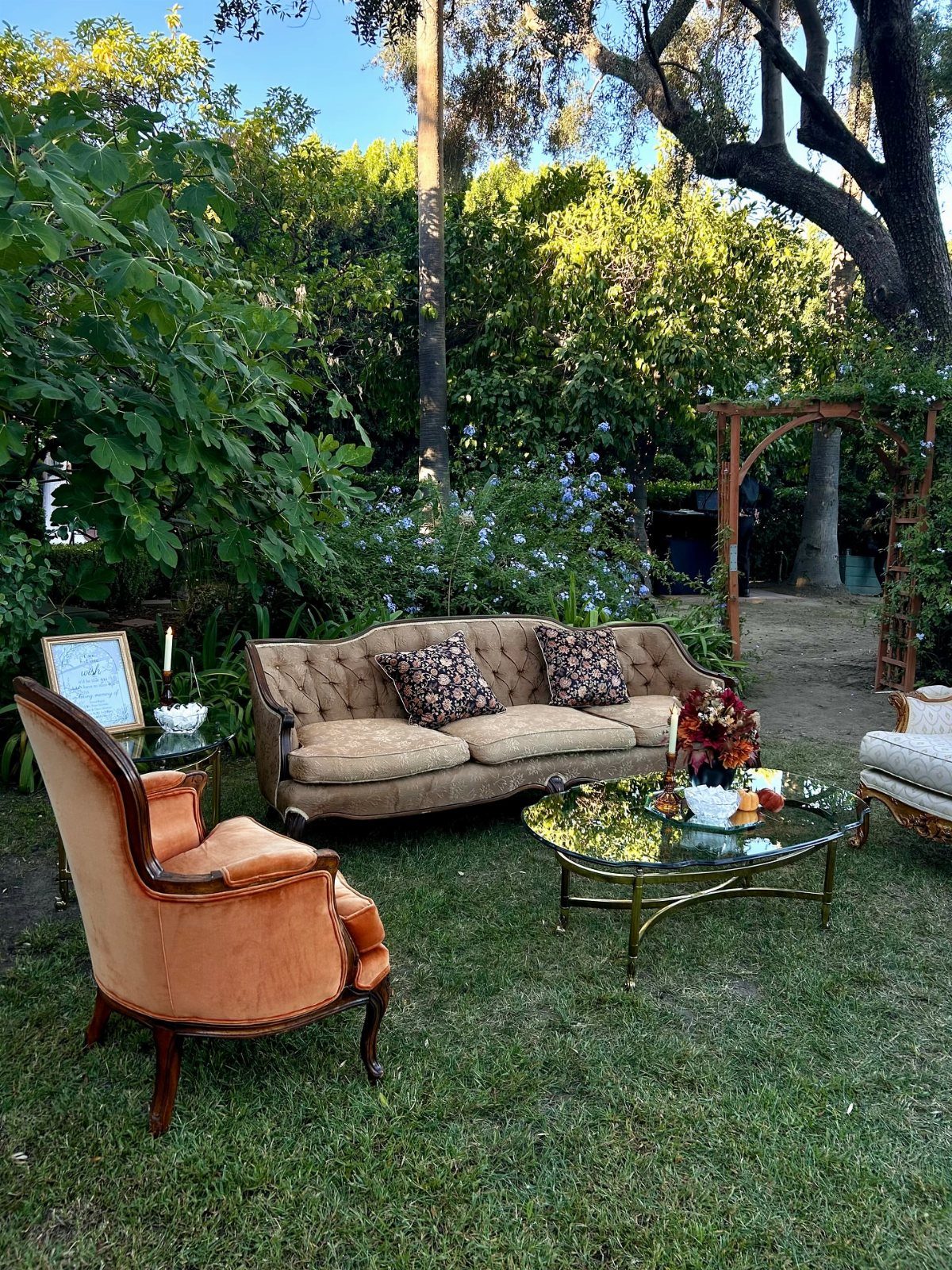 Vintage brown sofa and orange velvet armchair arranged as a lounge on grass.