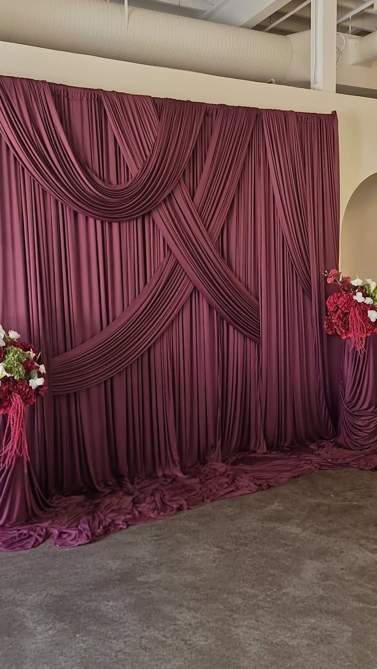 Burgundy red fabric draping backdrop with red and white floral accents.