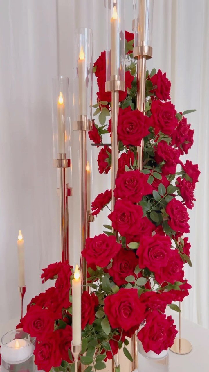 Red roses and lit white candles in gold holders as a wedding centerpiece