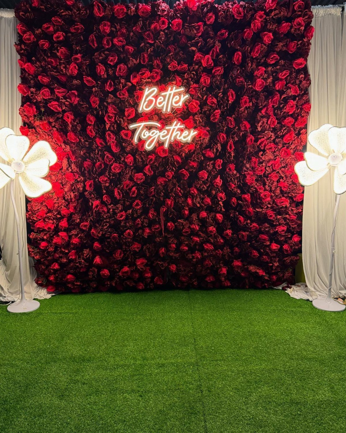 Red rose flower wall with a neon Better Together sign on green grass