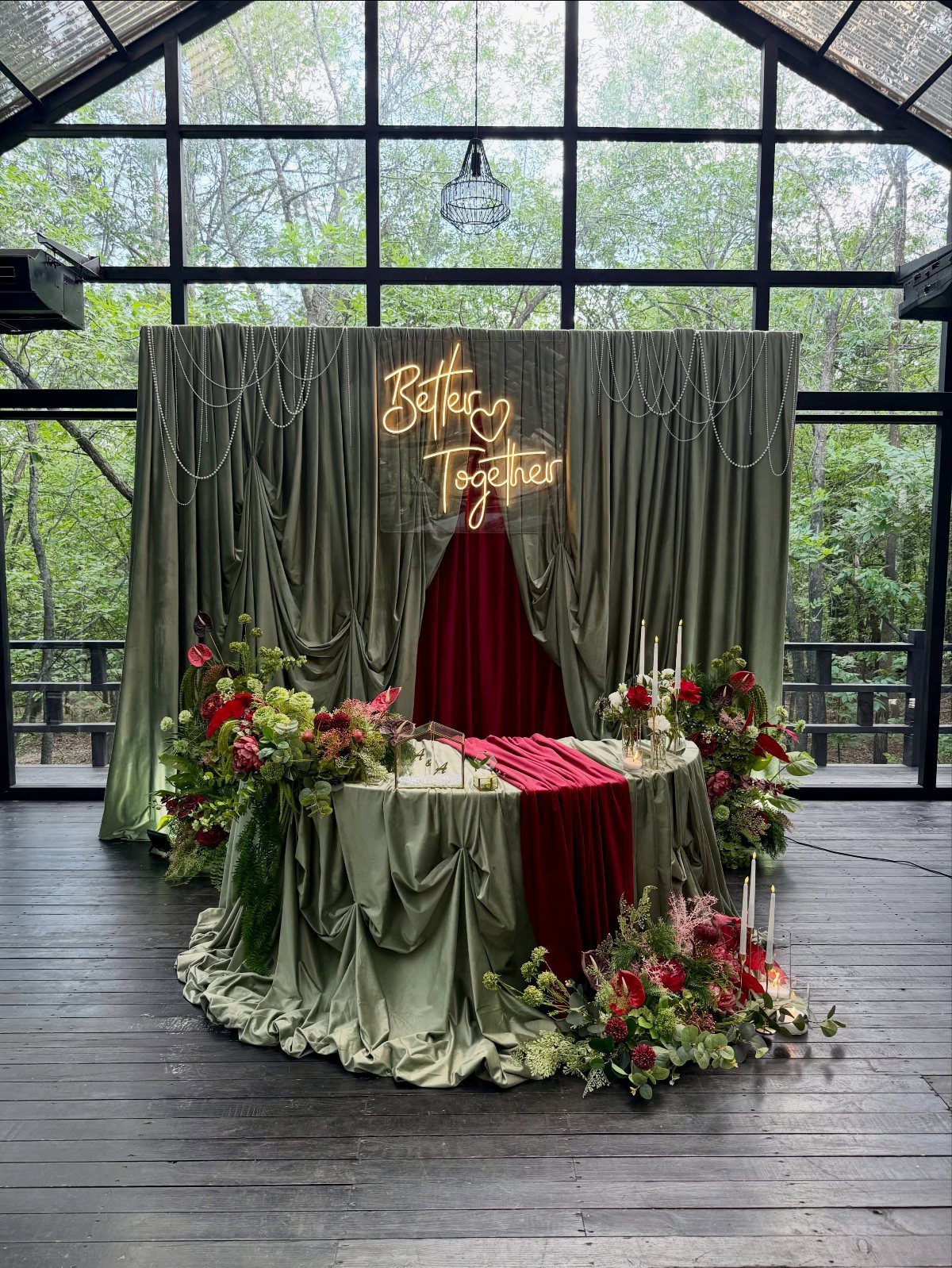 Olive green and red wedding decor with floral arrangements and a neon sign.