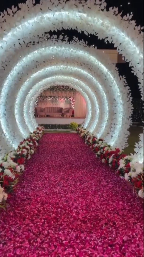 Red rose petals covering a wedding aisle under white floral arches