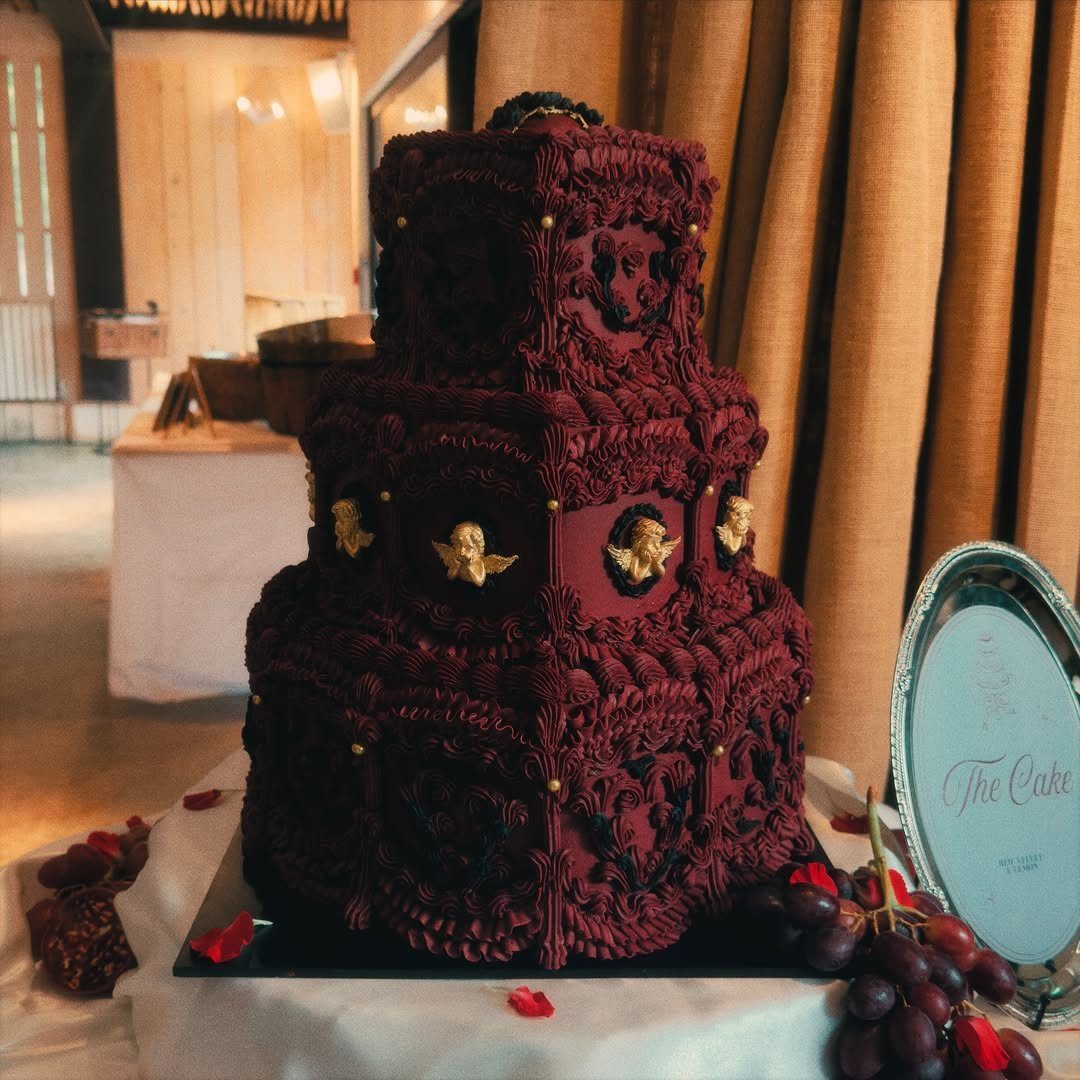 Ornate multi-tiered red velvet cake with gold accents and red grapes on table