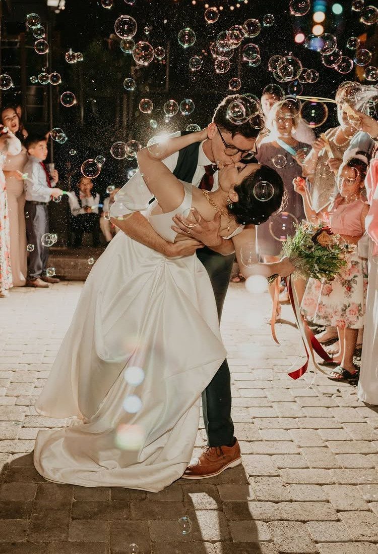 Bride and groom kissing in a dip surrounded by floating bubbles at night