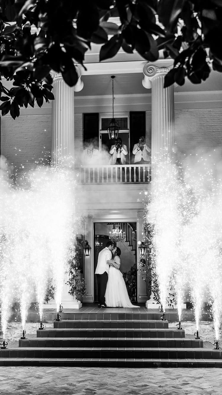 Bride and groom kissing on steps surrounded by tall vertical cold spark fountains