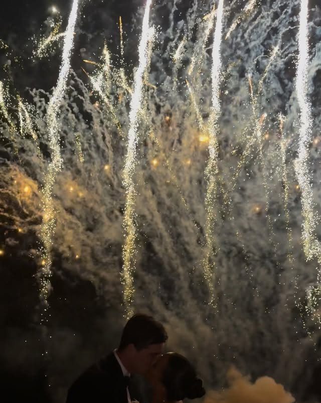 Couple kissing in silhouette against a backdrop of exploding white and gold fireworks.