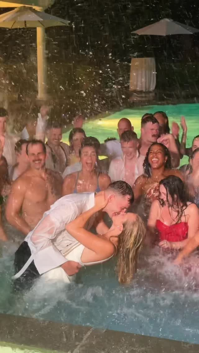 Bride and groom kissing in a swimming pool surrounded by cheering wedding guests