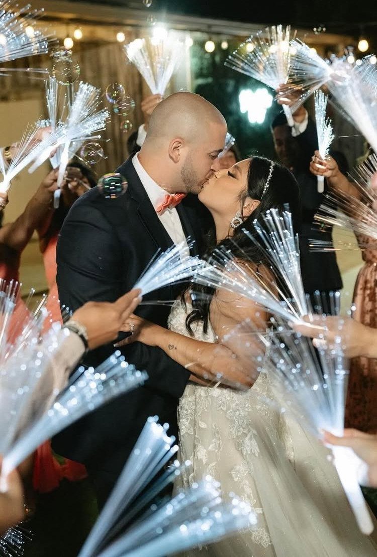 Bride and groom kissing while guests hold glowing white fiber optic wands around them.