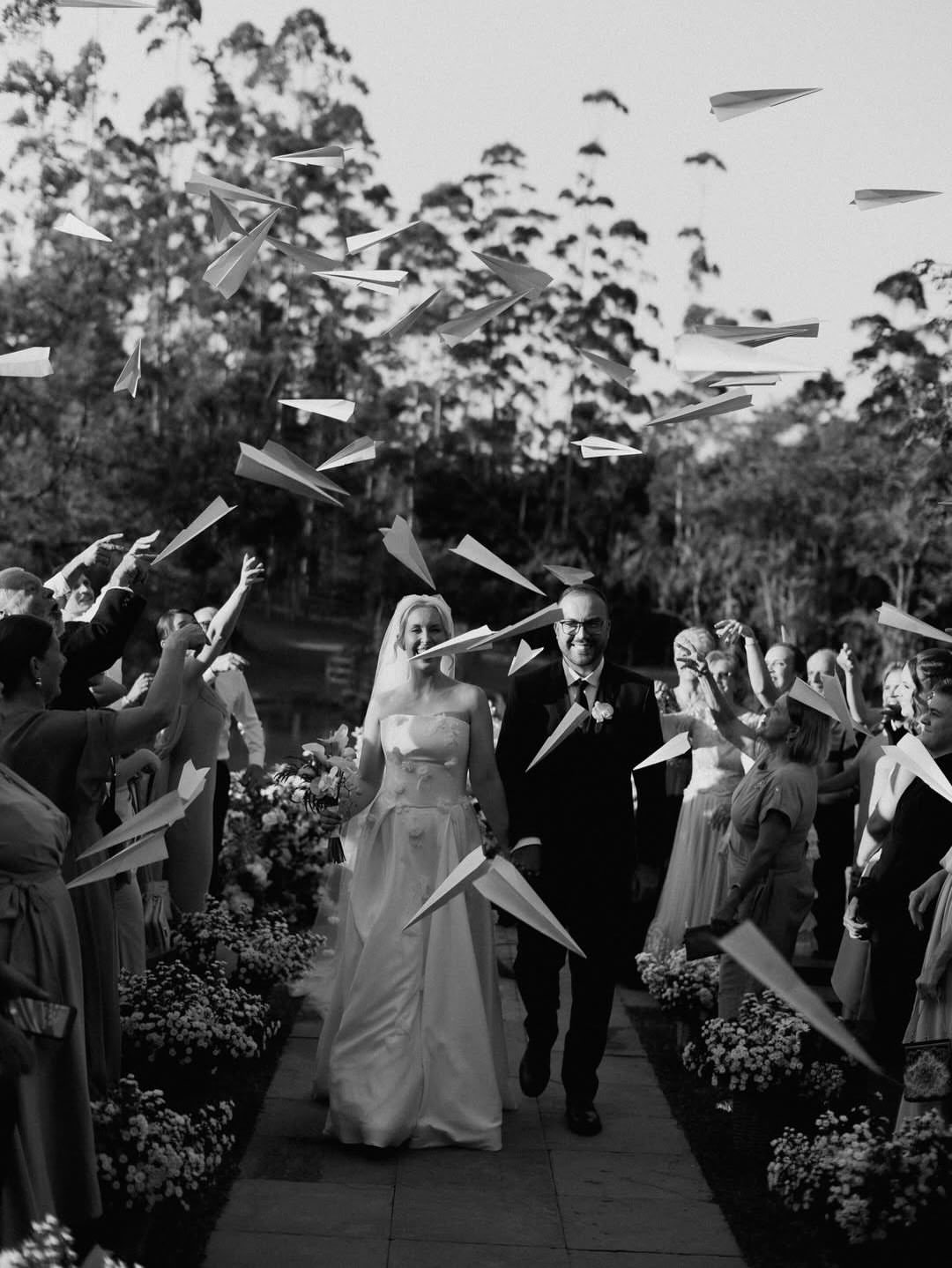 Bride and groom walking through guests tossing white paper airplanes in the air.