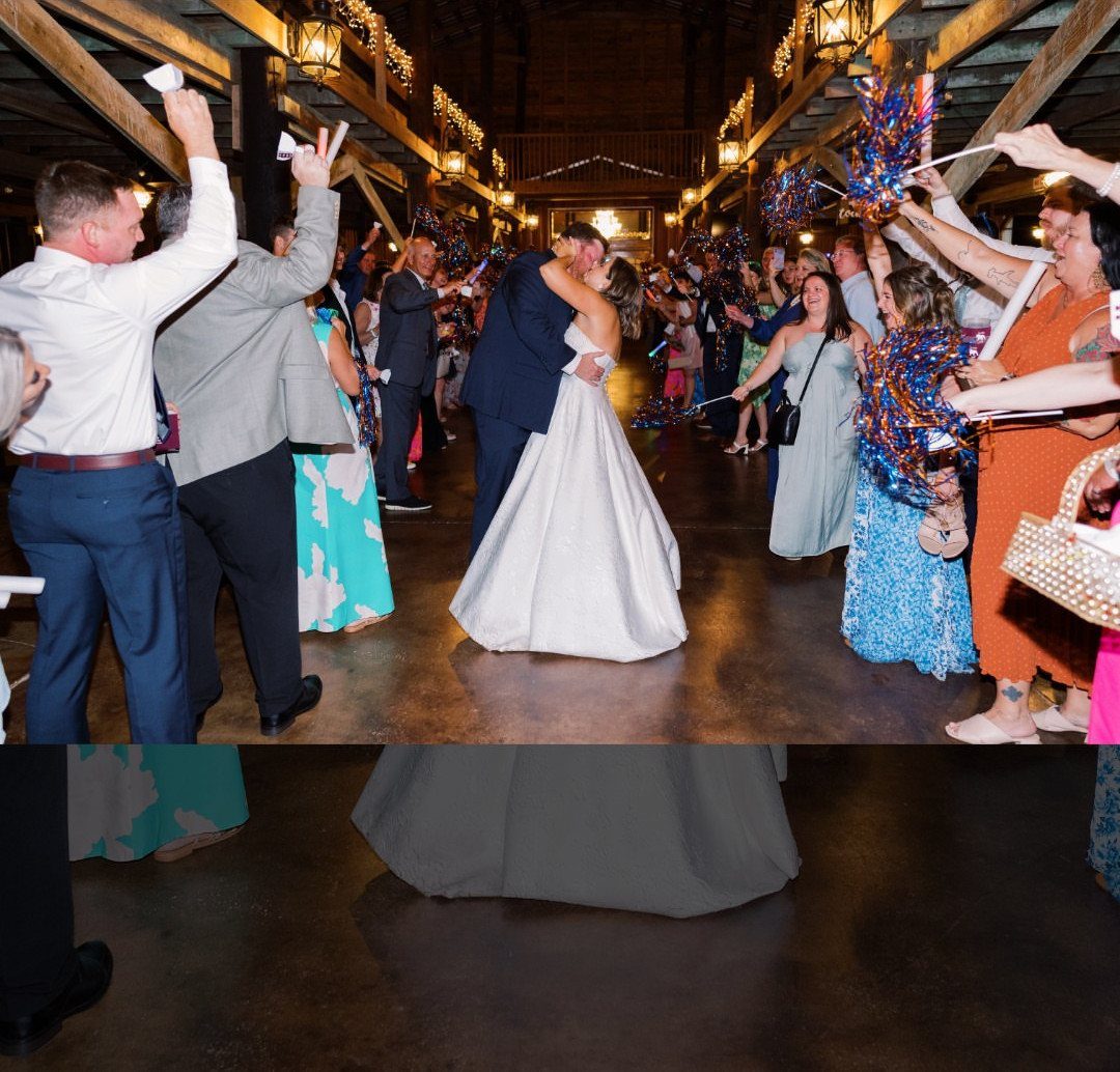 Bride and groom kissing while guests wave colorful pom poms in a rustic hall.