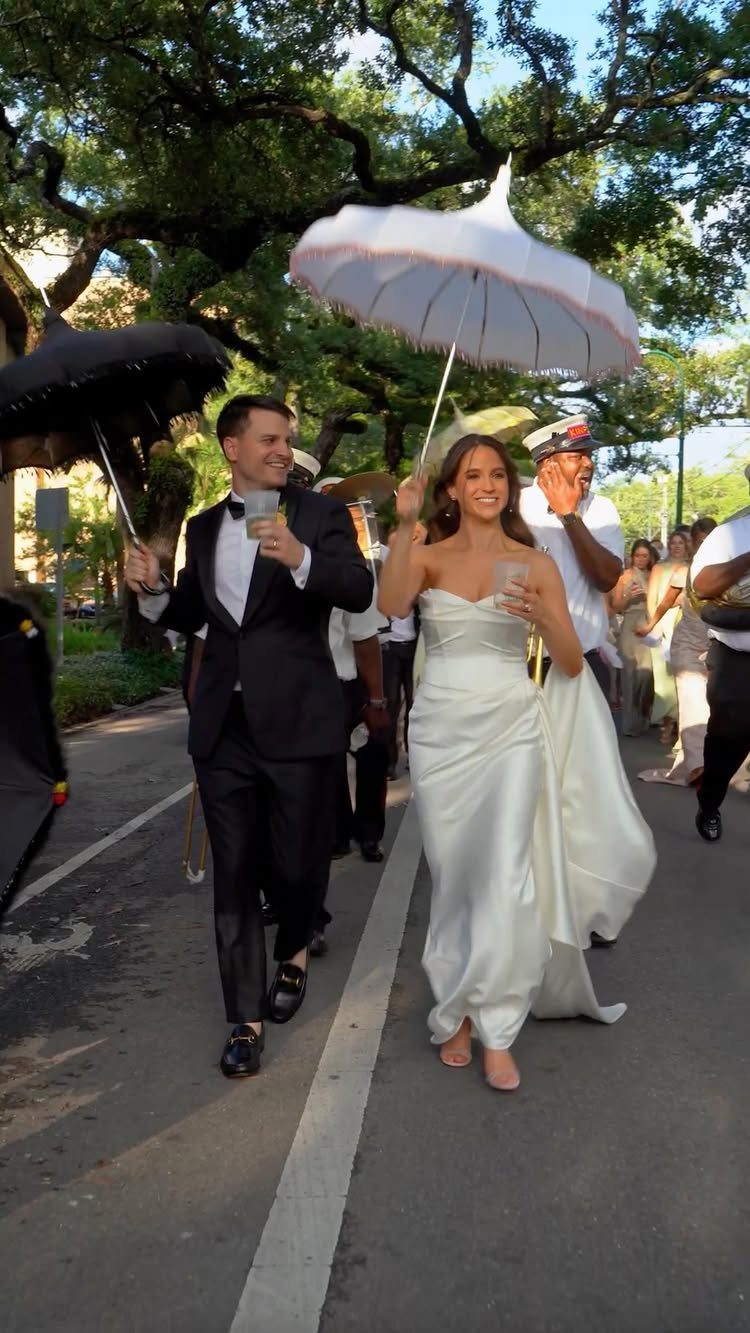 Bride and groom leading a festive second line parade with umbrellas and drinks.