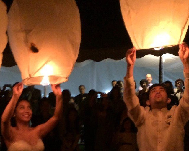 Bride and groom releasing glowing white sky lanterns during a nighttime wedding celebration.