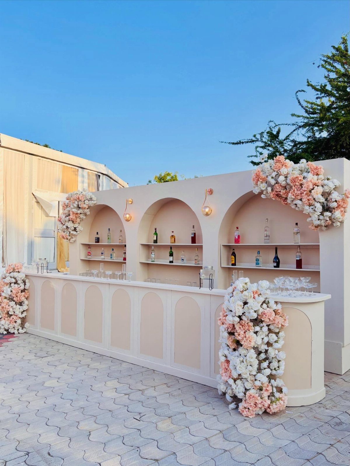 Cream outdoor bar decorated with peach and white rose floral arrangements and bottles.