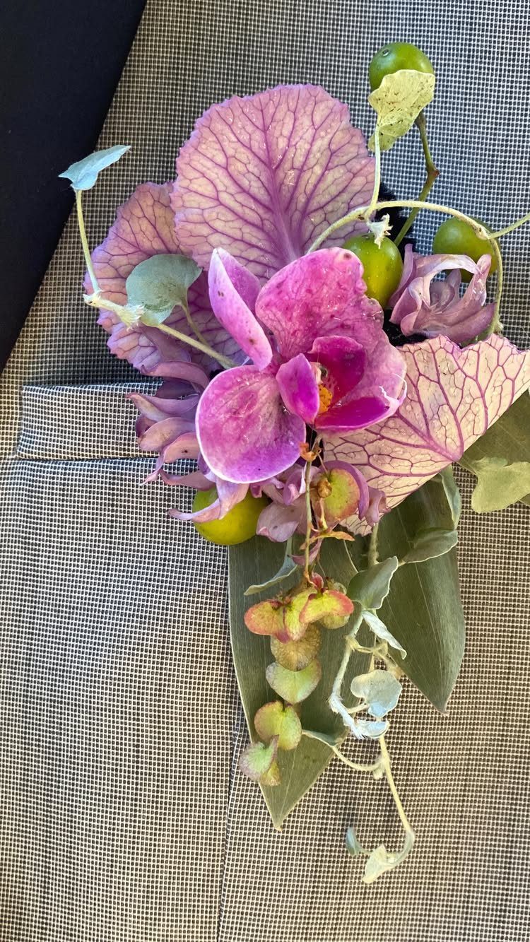 Floral boutonniere with purple orchid and skeleton leaves on a grey suit jacket