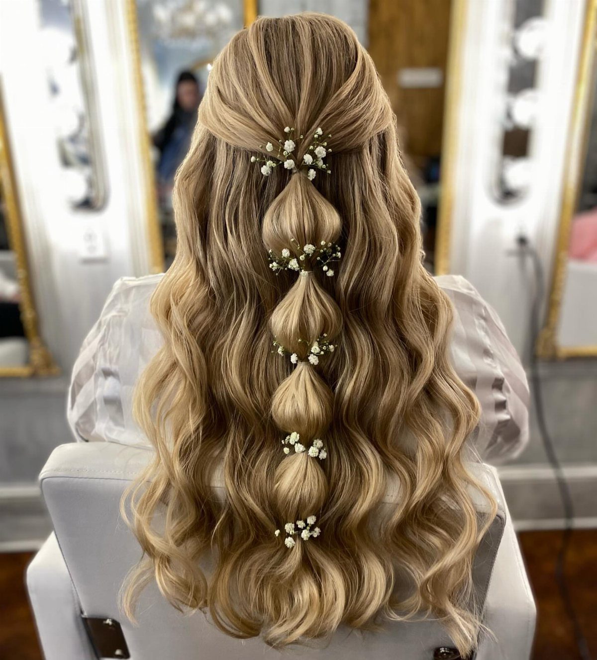 Long wavy blonde hair styled with small white flowers in a braided section.
