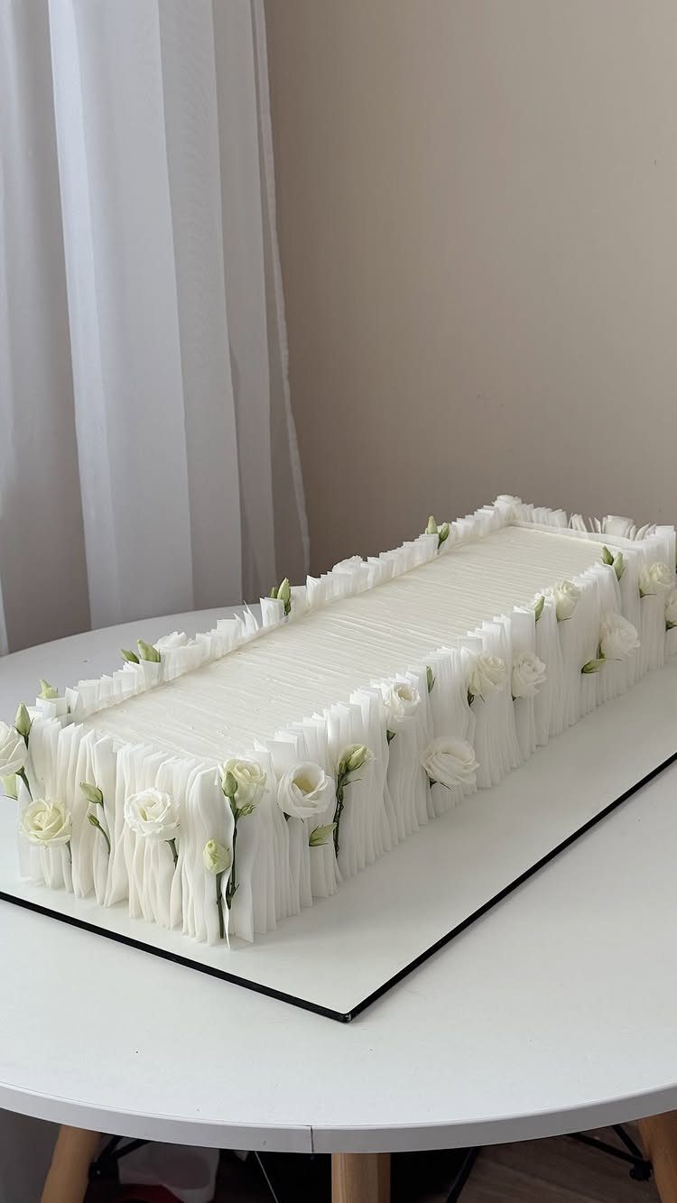 Rectangular white cake decorated with small white roses on a mirrored base.