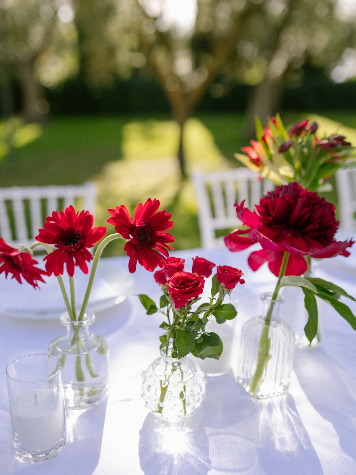Red flowers in small glass vases on a white tablecloth in a garden