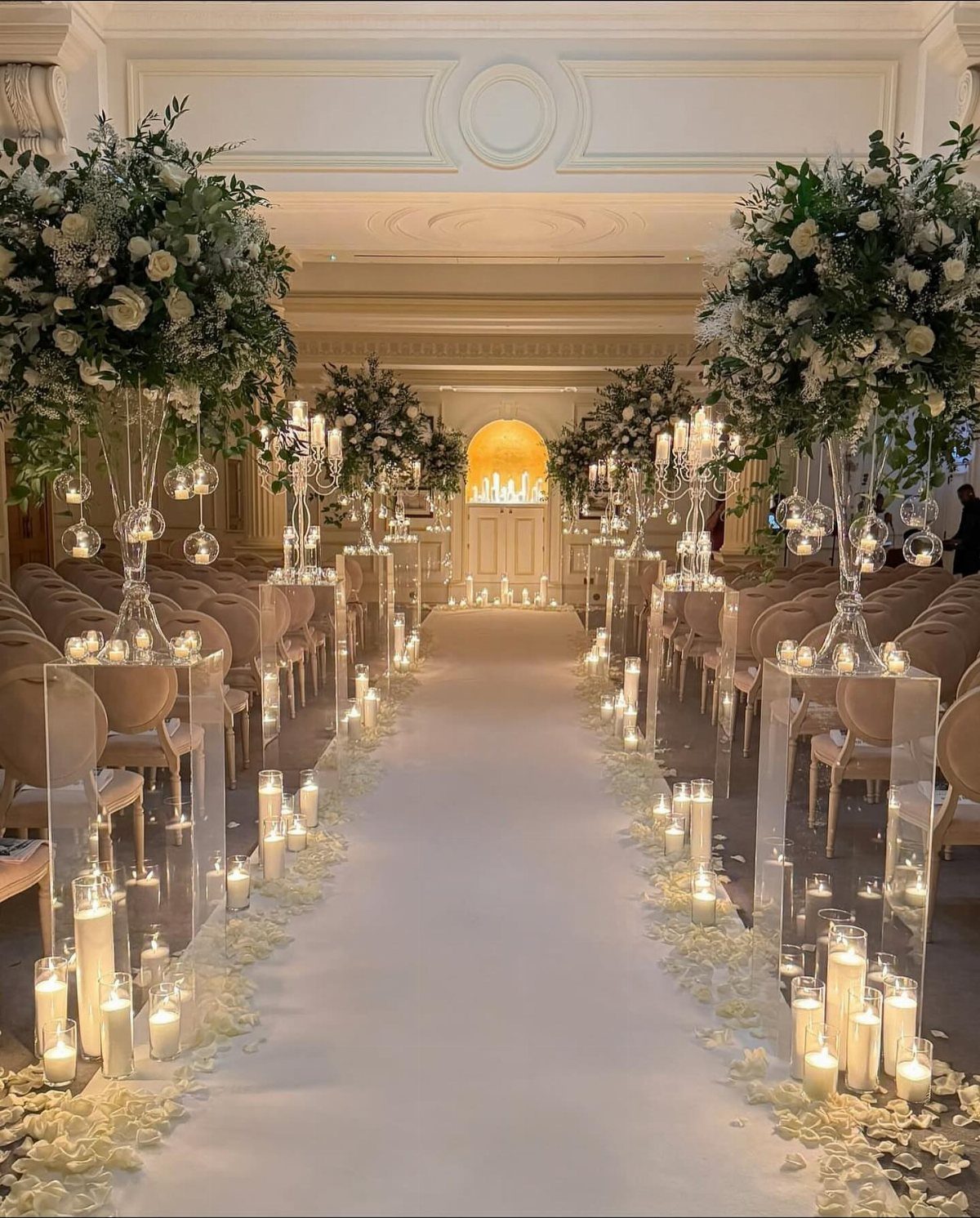 Wedding aisle with white flower petals, glowing candles, and tall floral centerpieces.