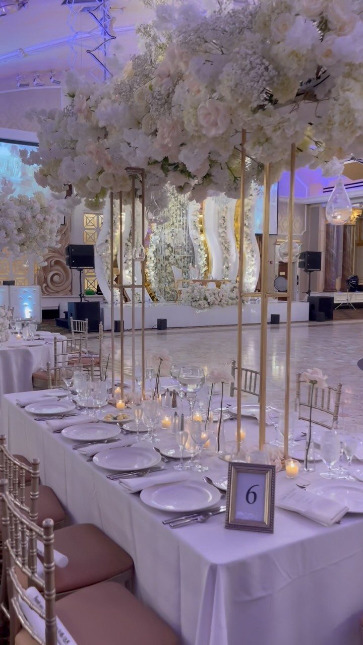 Tall white floral centerpieces on gold stands atop a decorated wedding banquet table.