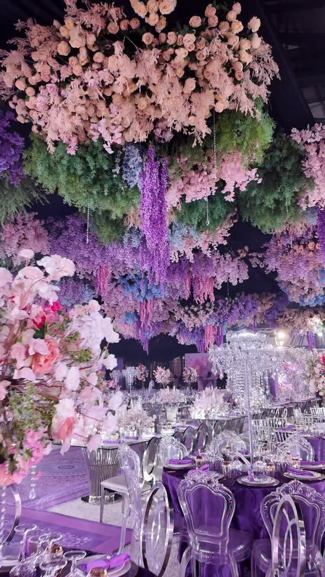 Lavish event hall with purple linens, crystal candelabras, and floral ceiling installations.