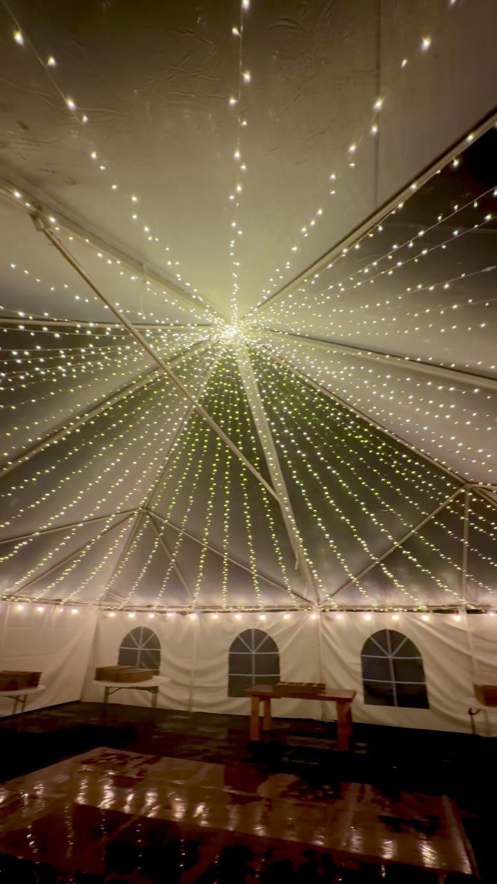 Warm white string lights radiating from the center of a white event tent ceiling.