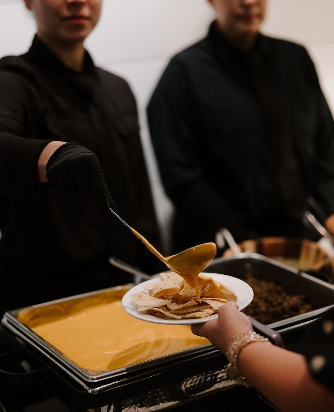 Cheese sauce being ladled over tortilla chips at a catered buffet station