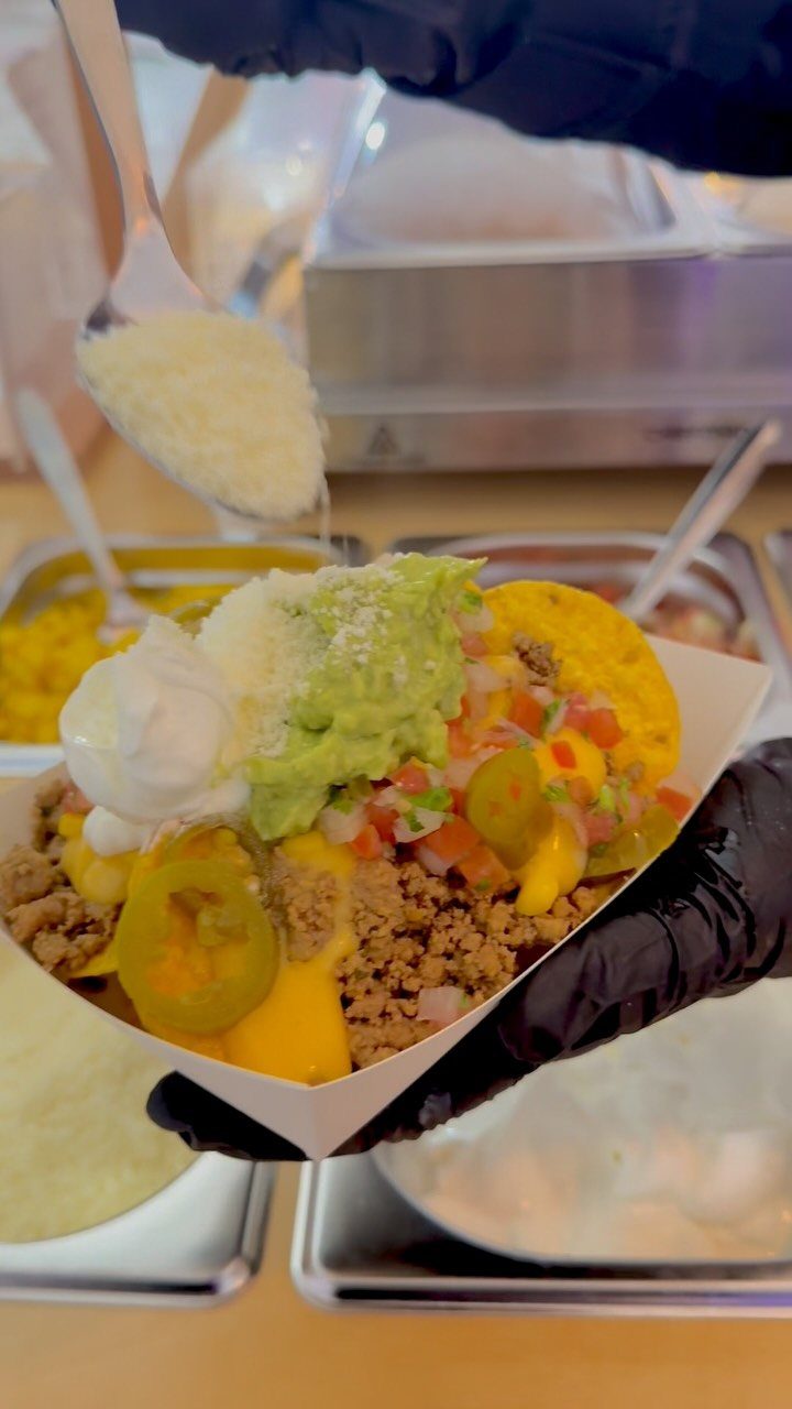 Nachos in a white tray topped with guacamole, sour cream, and grated cheese.
