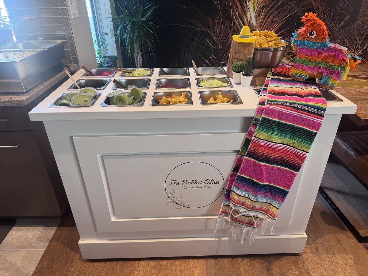 Nacho bar setup with toppings in metal trays and a colorful Mexican serape.