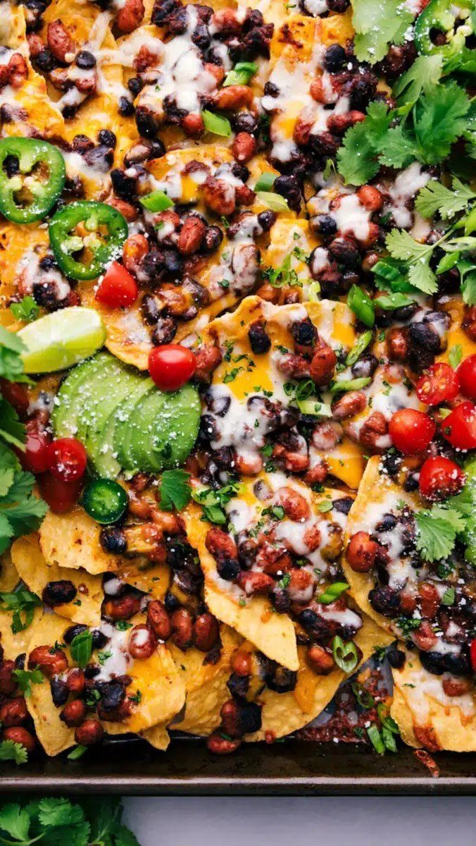 Nachos topped with melted cheese, beans, vegetables, and fresh cilantro on a tray