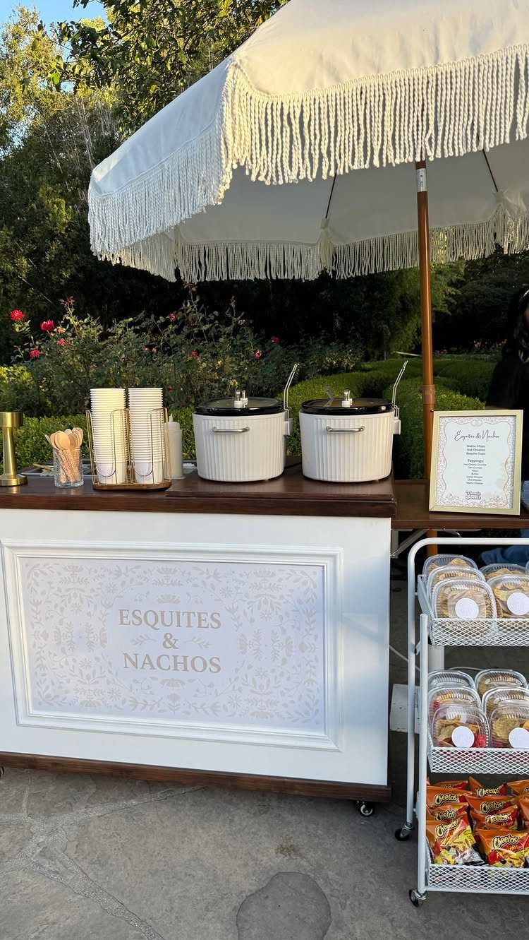 Nacho bar station with a white sign reading Esquites and Nachos under an umbrella