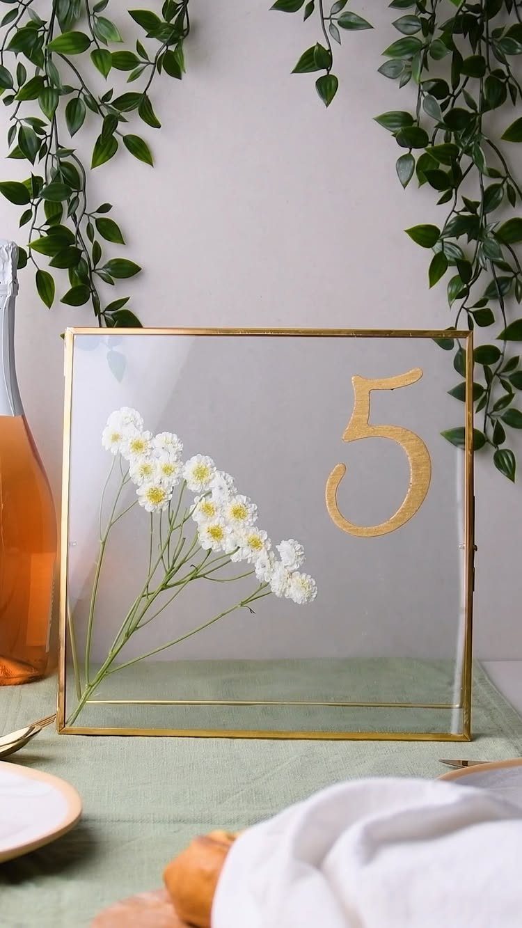 Acrylic table number five with gold frame and pressed white daisies on green tablecloth
