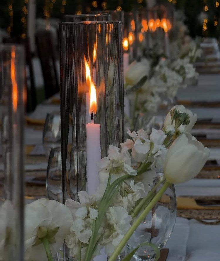 White candles in glass cylinders and white flowers on a wedding dinner table