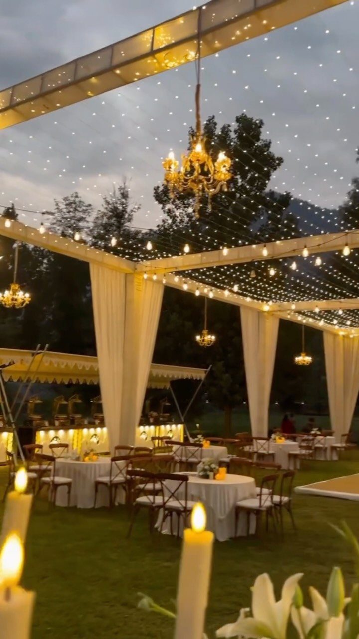 Outdoor wedding reception with white canopy, round tables, and twinkling fairy lights ceiling.