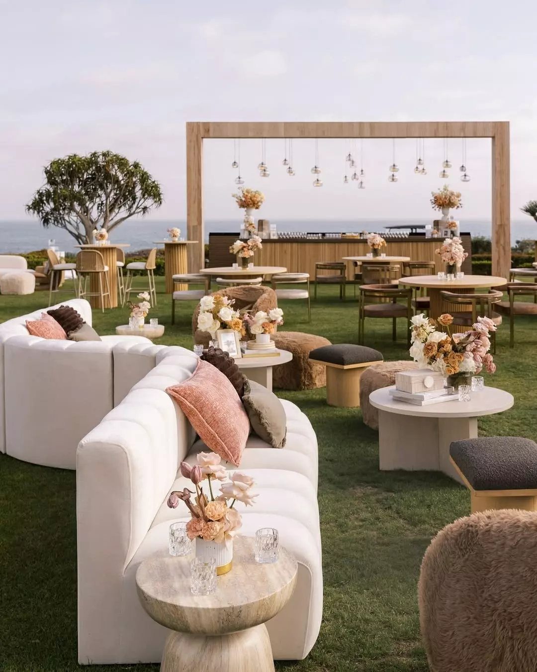 Outdoor wedding lounge area with white curved sofas and floral centerpieces on grass.