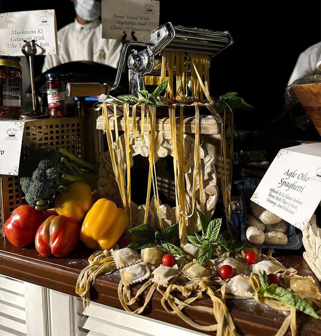 Pasta machine with fresh noodles and raw vegetables on a catering station counter