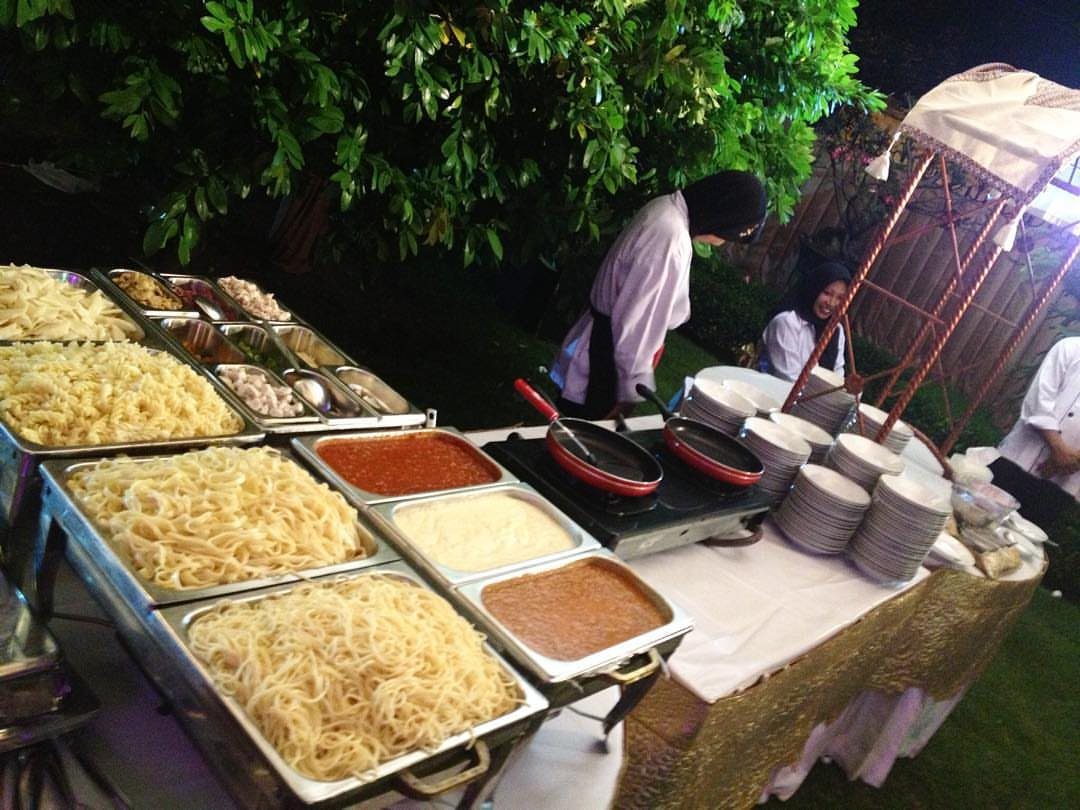 Pasta station with chafing dishes of noodles and sauces served by a chef.