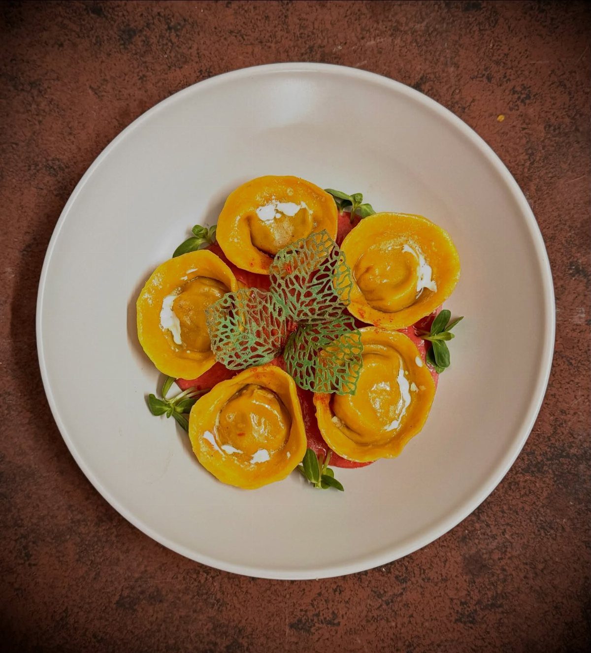 Yellow tortellini elegantly plated on a white dish with green garnishes and tuile.