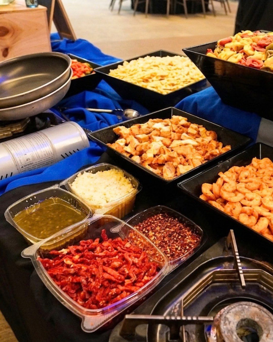 Catering spread featuring various pasta types, proteins, and toppings in black bowls.