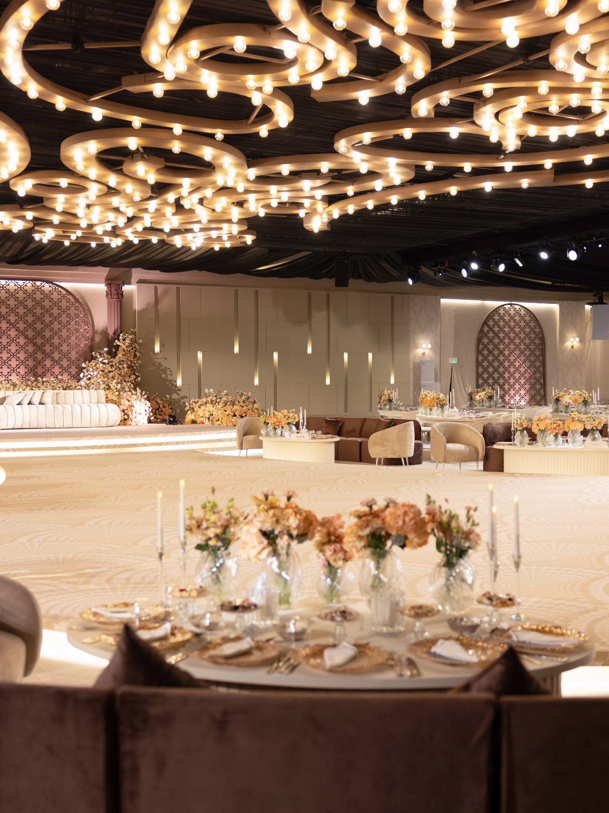 Swirling golden ceiling light installations above a luxury wedding reception dining area