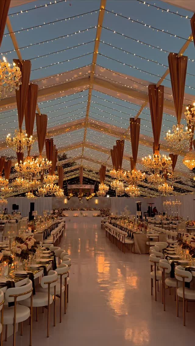 Ornate gold chandeliers and fairy lights illuminating a luxury wedding reception tent.