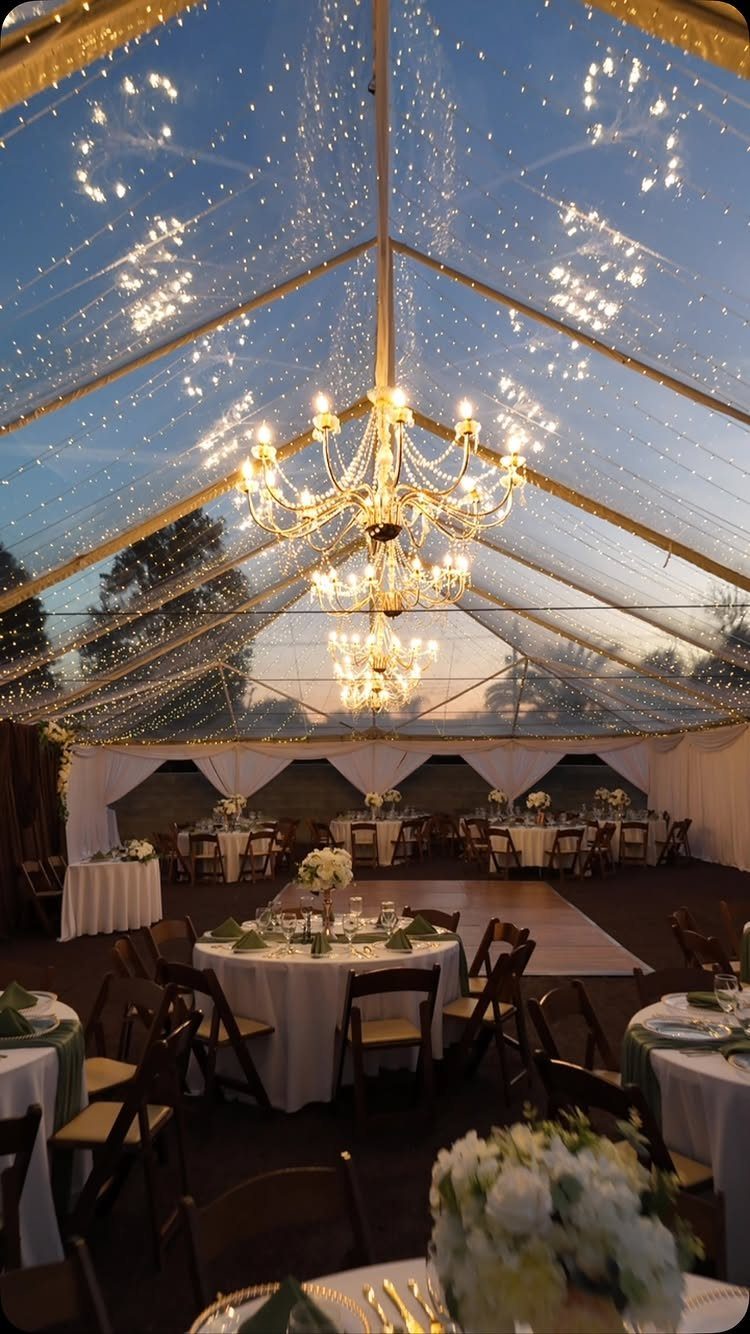 Crystal chandeliers and fairy lights illuminating a transparent wedding tent with dinner tables.