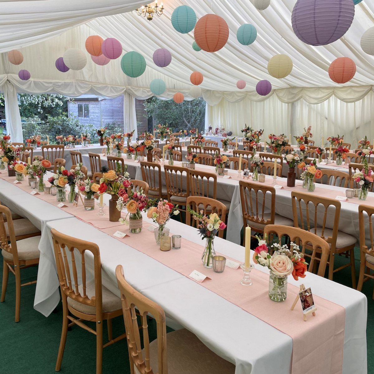 Colorful paper lanterns hanging from the ceiling of a wedding reception marquee tent.