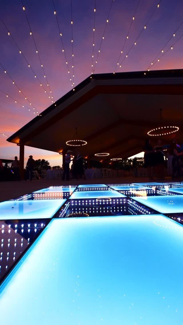 Glowing blue LED dance floor under a pavilion with overhead string lights.