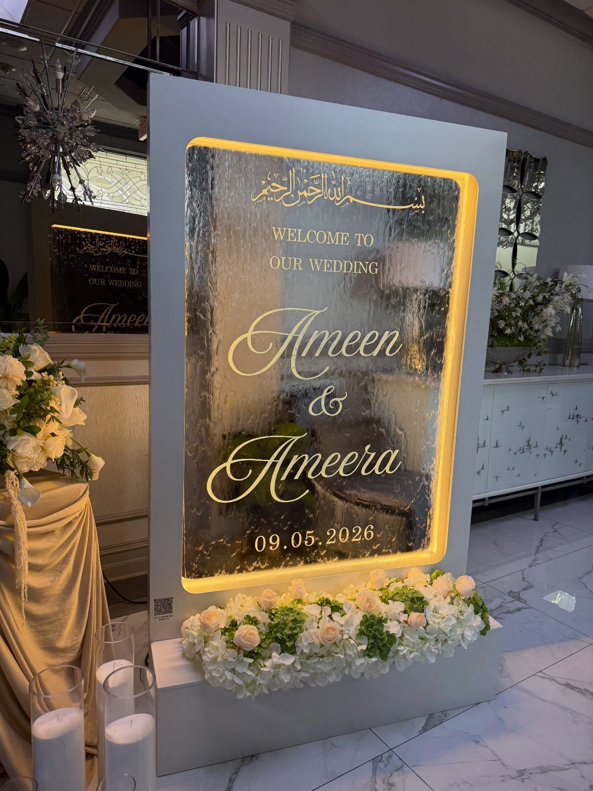 Lighted wedding welcome sign with mirrored center and white floral base arrangement