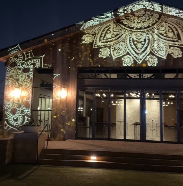 Mandala light patterns projected onto the wooden exterior walls of a venue at night.